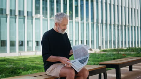 senior person reading newspaper on street. good looking mature man resting bench