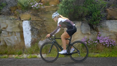 Female-cyclist-cycling-on-a-countryside-road-besides-the-rock-4k