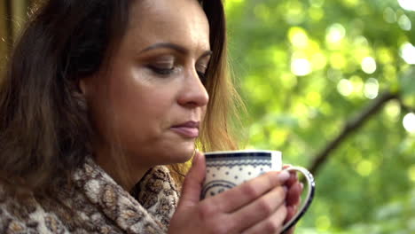 Close-up-FHD-shot-of-a-brunette-middle-aged-woman-enjoying-the-smell-of-a-fresh-hot-breakfast-tea,-holding-the-cup-with-both-hands