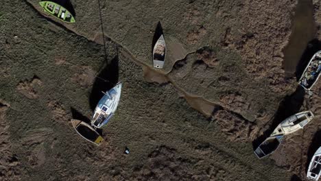 aerial view over various stranded abandoned fishing boat wreck shipyard in marsh mud low tide coastline