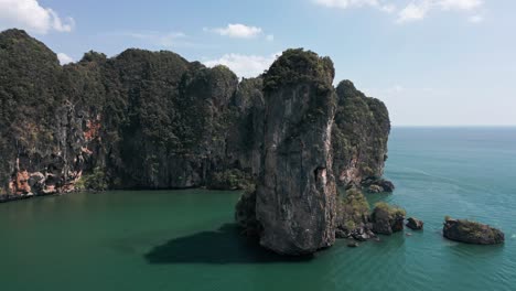 Aerial-pan-shot-of-tall,-giant-rock-standing-on-sea-at-Pai-Plong-Beach-with-limestone-cliffs-in-Krabi,-Thailand