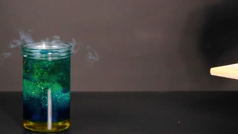 a vibrant liquid in a beaker reacts, producing swirling smoke and dynamic color changes.