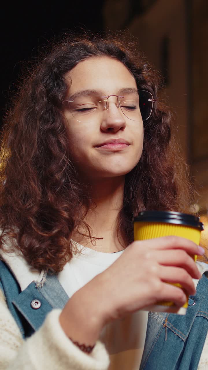 feliz joven sonriente disfrutando de café bebida caliente relajándose tomando un descanso en la calle de la ciudad de la noche