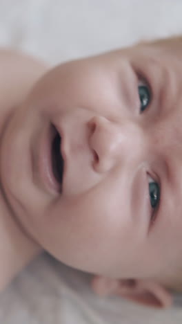 adorable infant with crystal blue eyes and blond hair lies in baby bed looks at camera and starts crying extreme closeup