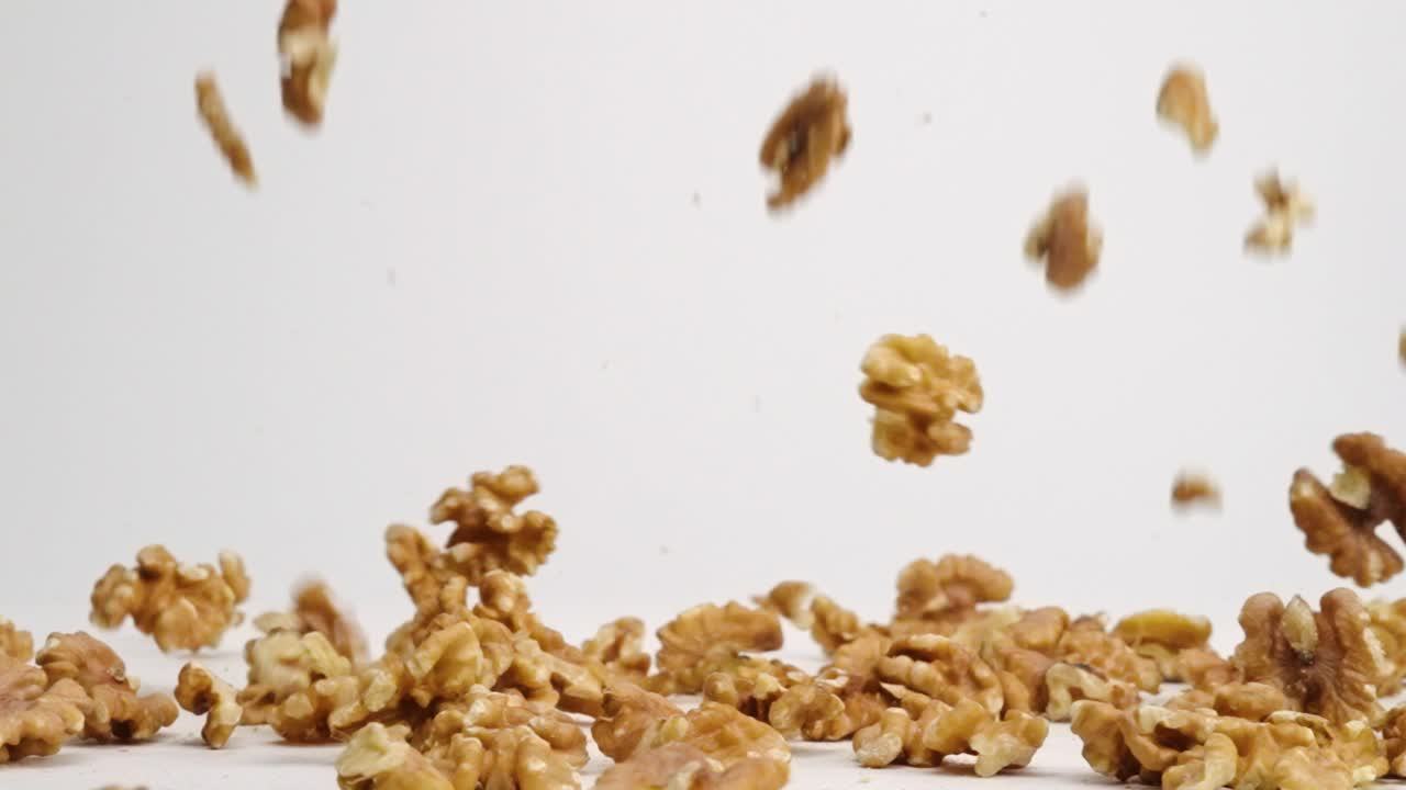 Whole walnut pieces falling onto white table top and bouncing around before landing in a pile in slow motion