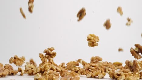 whole walnut pieces falling onto white table top and bouncing around before landing in a pile in slow motion