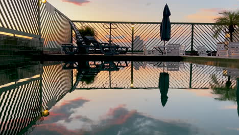 escena tranquila del cielo de la puesta de sol reflejada sobre la superficie de una piscina en la azotea, tiro estático