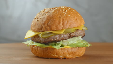 la hamburguesa gira en una tabla de madera. una hamburguesa con un queso de ensalada y tomates gira contra una pared gris