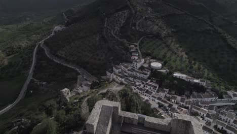 4k bird’s-eye drone shot of zahara de la sierra, spain, filmed with a dji at 30fps. a cinematic backward flight revealing the stunning medieval castle atop the mountain.