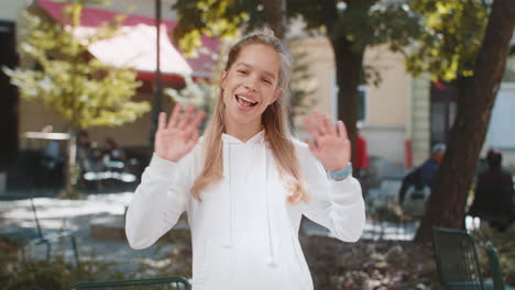 cheerful young woman tourist smiling at camera waving hands gesturing hello standing on city street