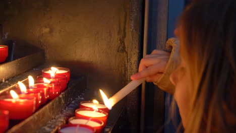 Close-up-of-a-beautiful-blonde-girl-lighting-candles-carefully-in-a-church