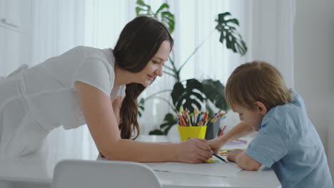 Joven-Y-Hermosa-Madre-E-Hijo-Dibujan-Con-Lápices-De-Colores-Sentados-En-La-Mesa-De-La-Cocina.-La-Cámara-Se-Mueve-En-Cámara-Lenta