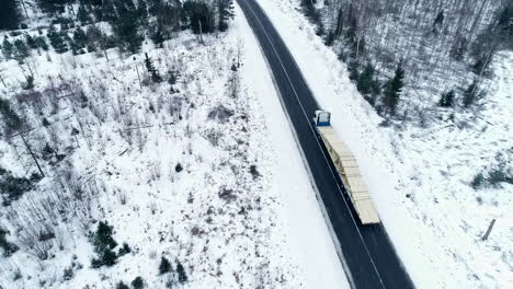 Aerial-drone-shot-of-long-lorry-driving-on-a-road-in-the-middle-of-forest-in-winter