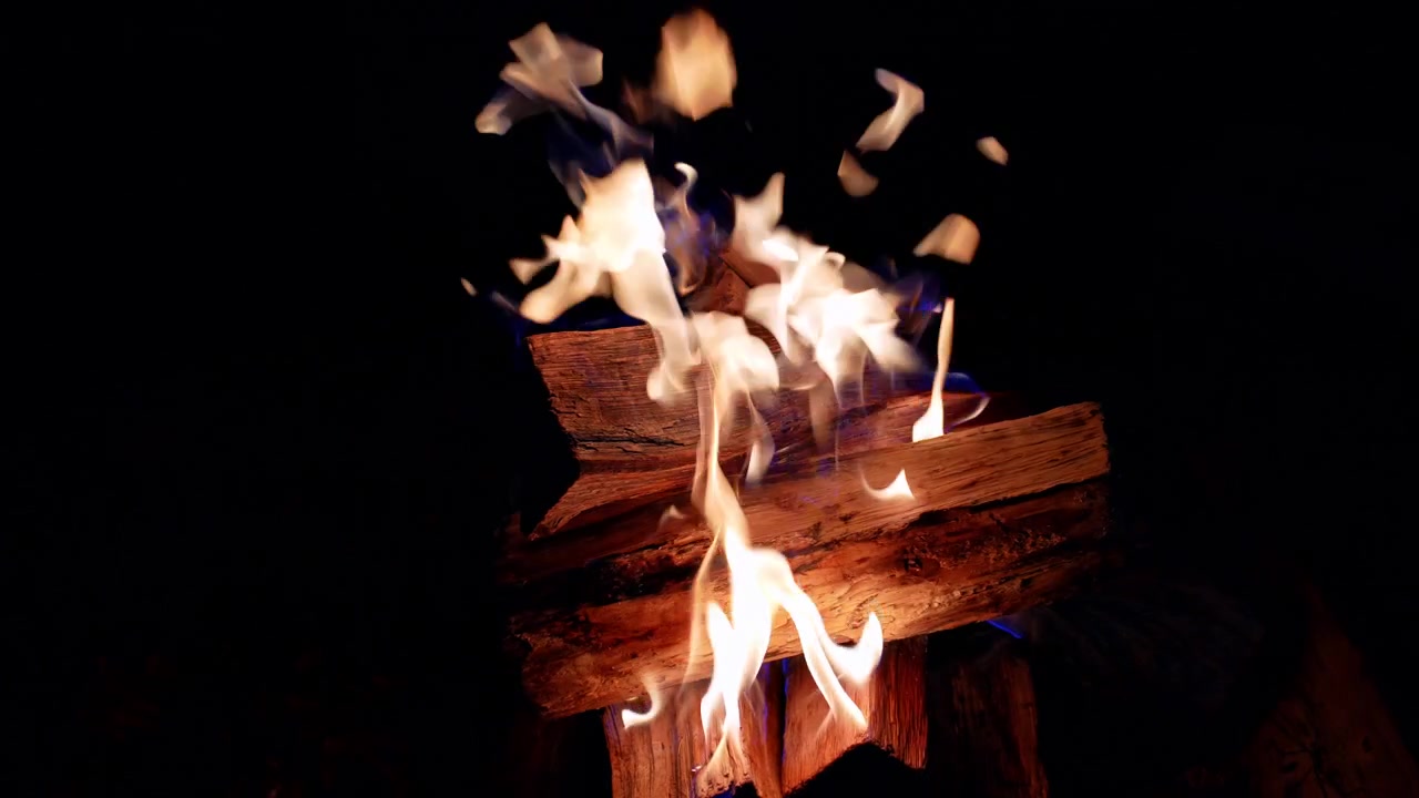 Fiamme vivaci che si alzano da ceppi di legno ardenti di notte. Dettaglio di fiamme gialle e arancioni che tremolano su ceppi di legno carbonizzati nell'oscurità.