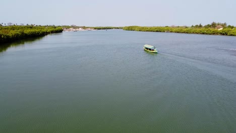 aerial drone shot of a river in gambia while a green sailing boat swimming forward with a view of landscape in kartong on sunny summer day