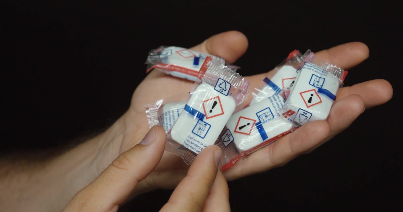 Primo piano di bustine di gel di silice disidratante tenute in mano. Ideale per la protezione dall'umidità, l'imballaggio, la spedizione, lo stoccaggio e la conservazione dei prodotti