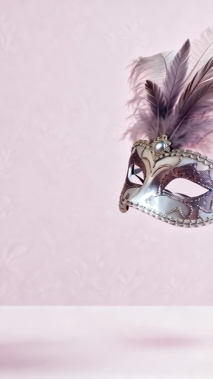 Video verticale: Maschera decorata entra da destra e si sposta a sinistra su una mensola rosa, mettendo in mostra piume e nastro.