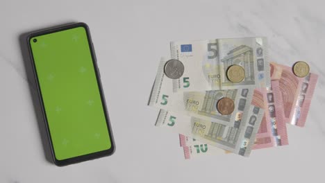 Überkopfaufnahme-Einer-Person,-Die-Euro-Banknoten-Und--Münzen-Neben-Einem-Greenscreen-Handy-Ablegt-1