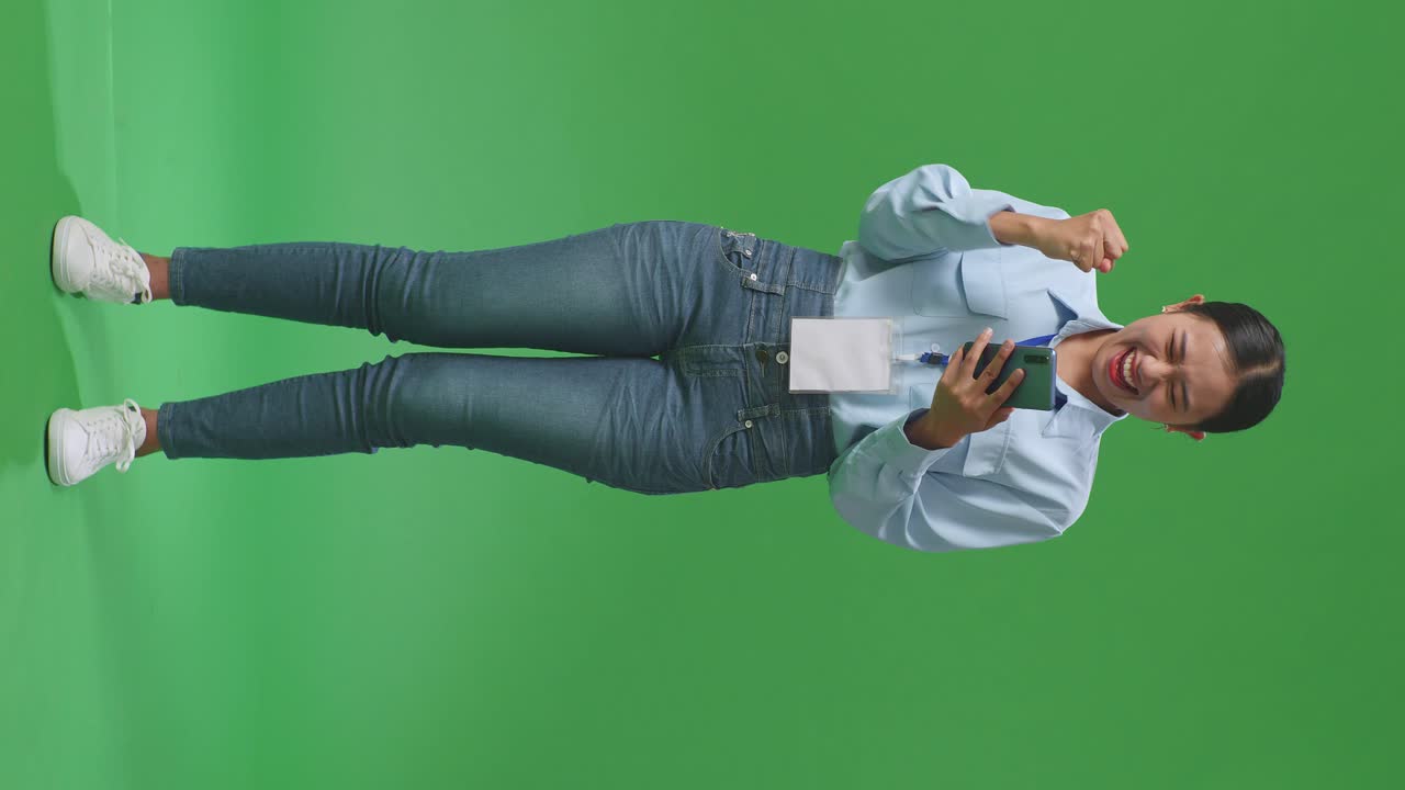 Full Body Of Happy Asian Business Woman Celebrating Using Mobile Phone On Green Screen In The Studio