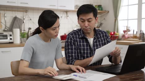 asian married couple calculating budget bill on calculator in dining room at home.