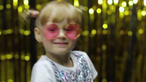 Child-kid-dancing,-claping-her-hands,-fooling-around.-Girl-posing-on-background-with-foil-curtain