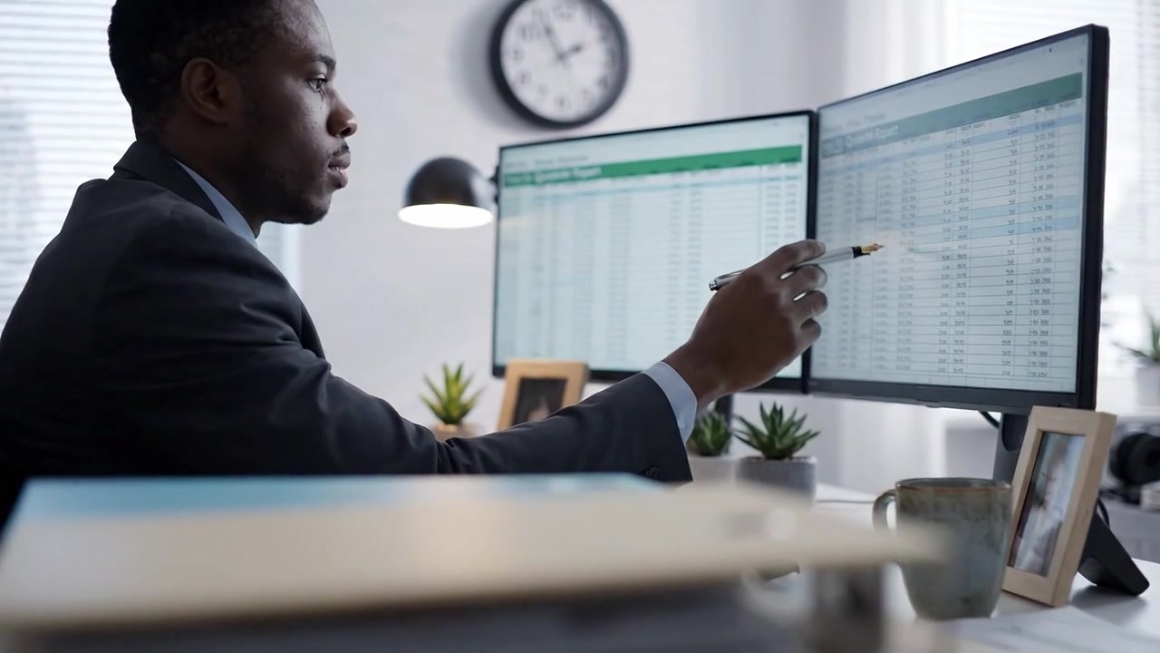 Profesional Berfokus Menganalisis Data di Dua Monitor di Lingkungan Kantor Modern dengan Sentuhan Pribadi dan Organisasi yang Efisien untuk Produktivitas