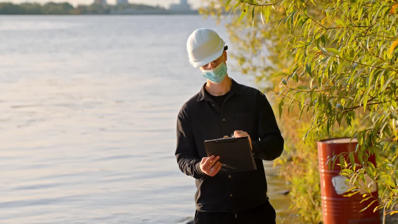 Engineer wearing mask and helmet taking notes during river inspection
