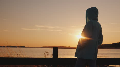 Silueta-De-Mujer-Solitaria-Sentada-Junto-A-La-Valla-Admirando-La-Atardecer-Sobre-El-Lago