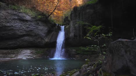 water falls down corner of rocky ledge in kemptner tobel forest, autumn foliage in wetzikon switzerland