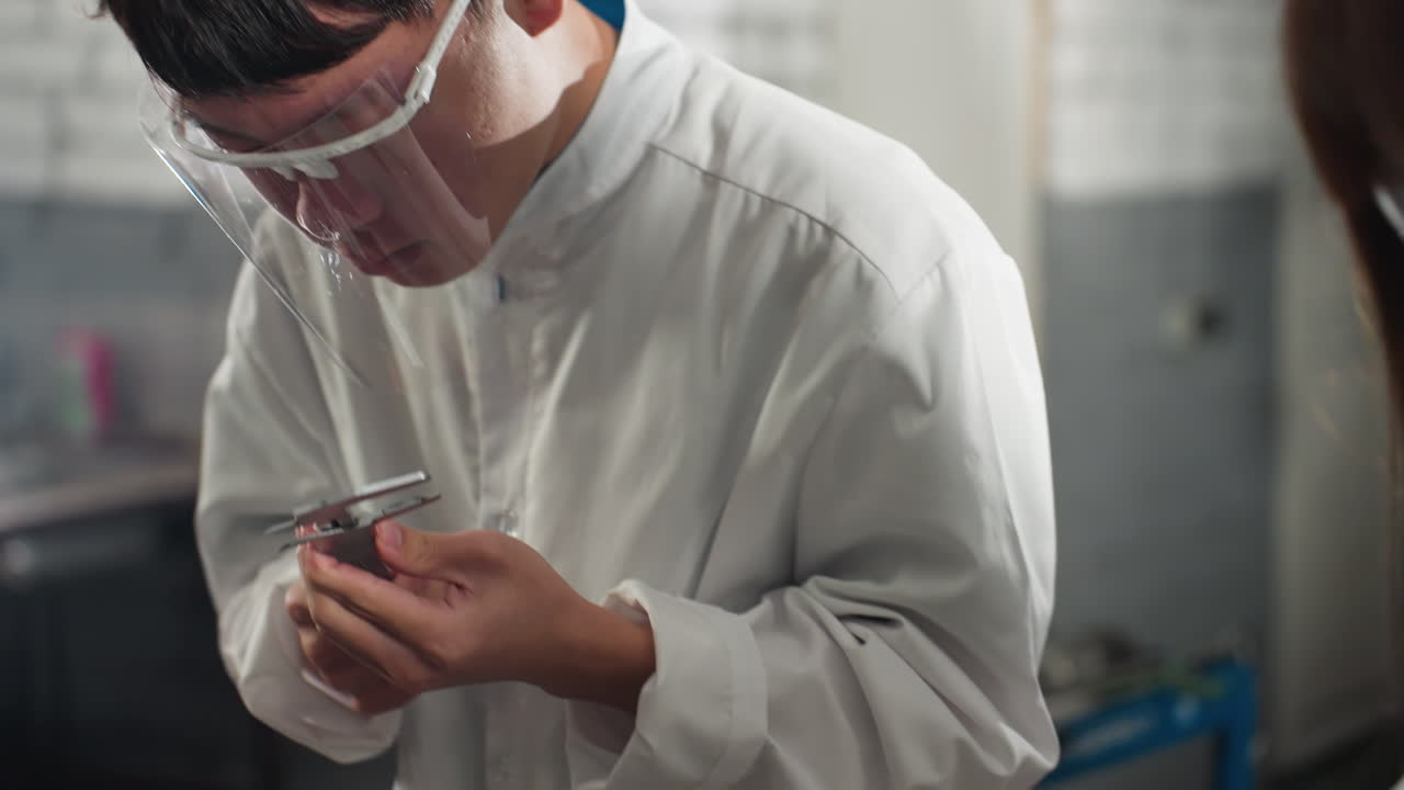 Close-up of lab technician in Chinese automotive workshop, reviewing measurement data with vernier caliper while discussing with colleague nearby, bright light illuminates workspace