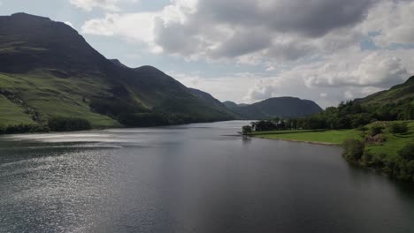 Low-drone-shot-flying-backward-over-Crummock-Water-on-a-sunny-day,-Lake-District,-Cumbria,-UK