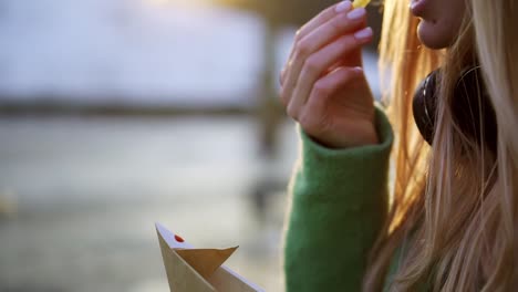 Woman-eating-french-fries-outdoors-on-winter-street-dip-in-ketchup,-closeup