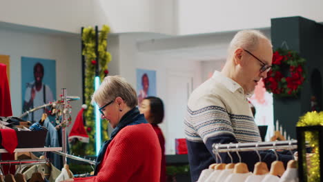 una pareja de ancianos feliz después de encontrar el regalo de navidad ideal para su hijo mientras compran en una tienda de ropa decorada con xmas. clientes navegando por la ropa durante la temporada de vacaciones de navidad