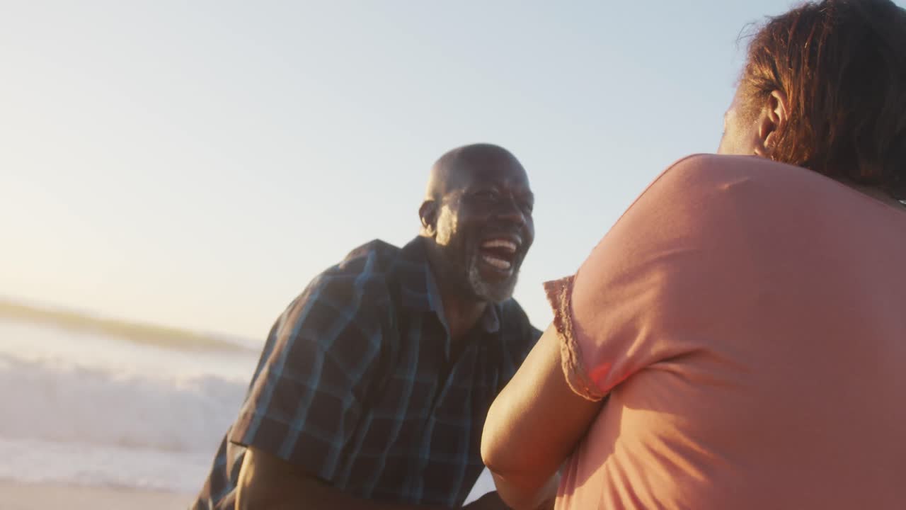 una pareja afroamericana de alto nivel sonriendo tomados de la mano y bailando en una playa soleada