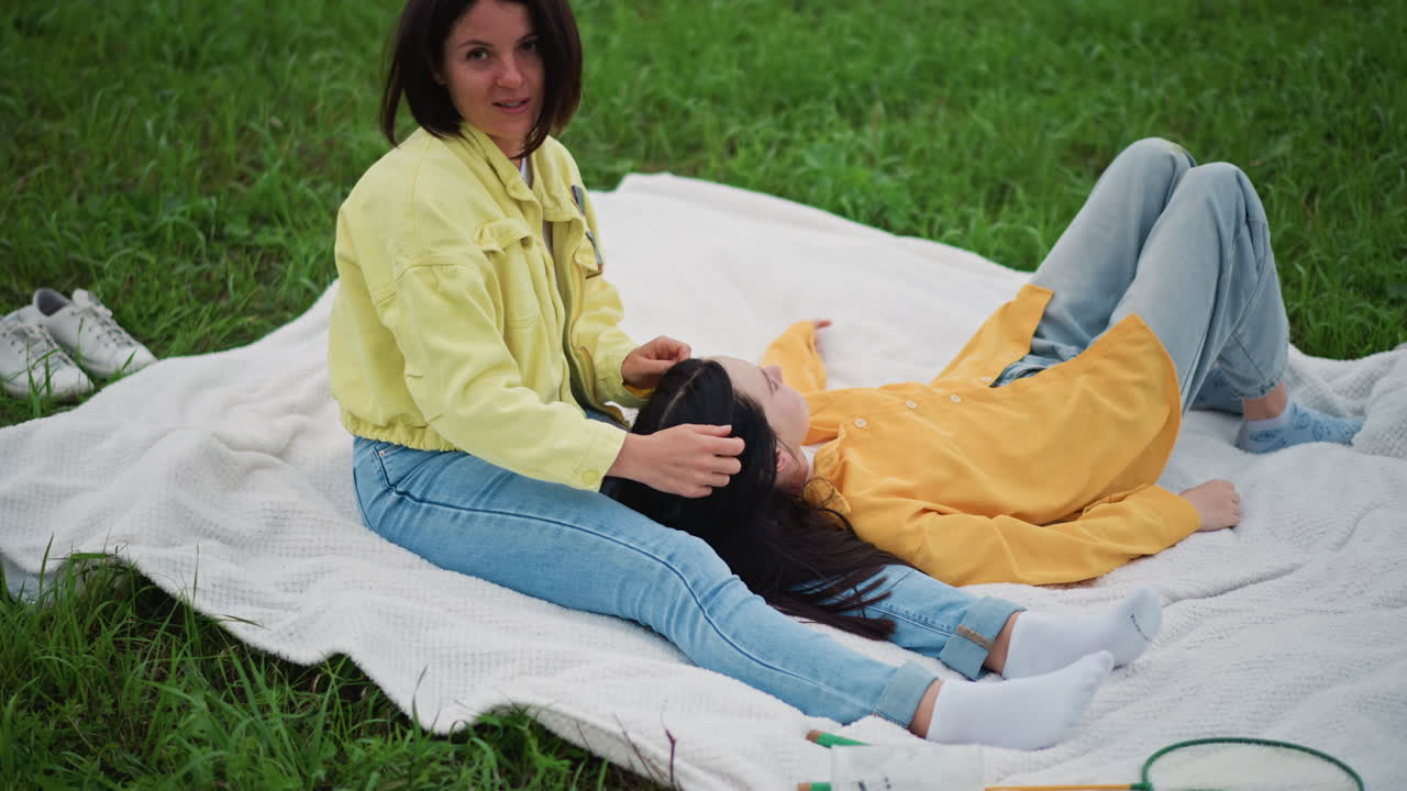 Donne gentili che condividono momenti di riposo, pacifico ritrovo all'aperto di donne che si rilassano su una coperta sotto il sole, scena serena con donne su una coperta da picnic immerse nella tranquilla atmosfera di un parco erboso