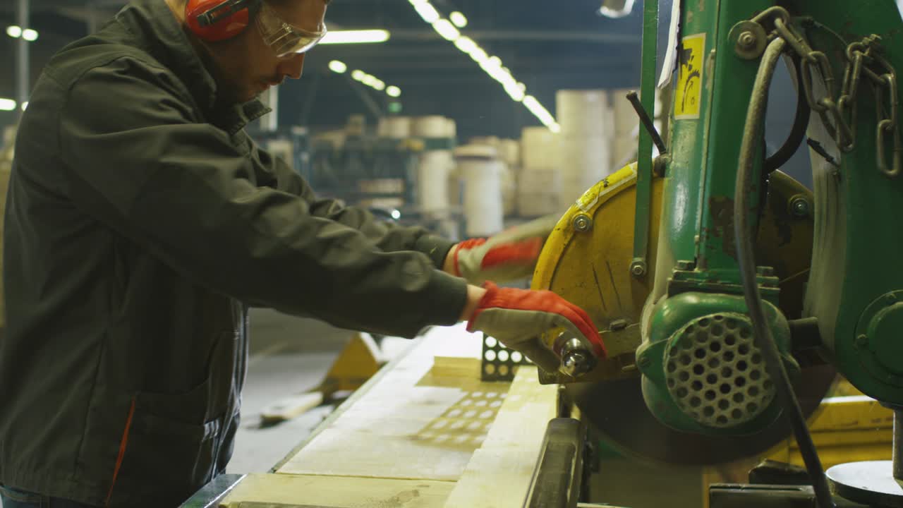 Lumber mill worker is cutting wood with circular saw.