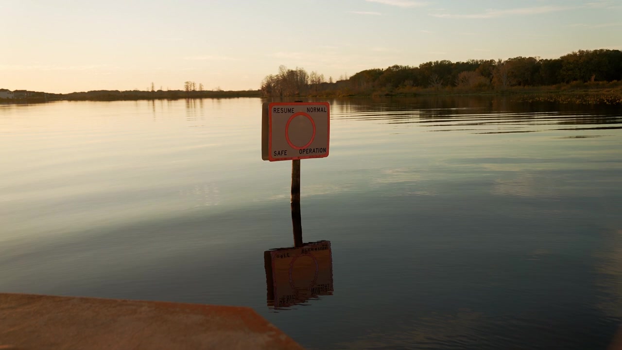 "Resume Normal Safe Operation" boating sign reflected in the calm sunrise waters of Lake Minneola in Clermont, Florida, with a peaceful shoreline in the distance.