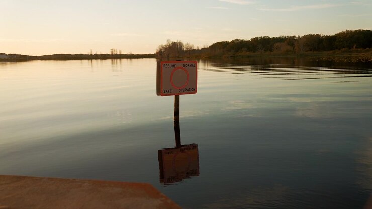 Cartello nautico "Riprendere la normale operazione sicura" riflesso nelle calme acque all'alba del lago Minneola a Clermont, Florida, con una tranquilla costa in lontananza
