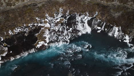 aerial view rising away from the snowy hraunfossar waterfall, in cloudy iceland