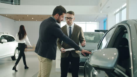 car salesman discussing car features with customer in showroom
