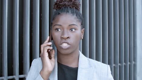 static shot of a smiling african-american businesswoman standing outside and talking on mobile phone