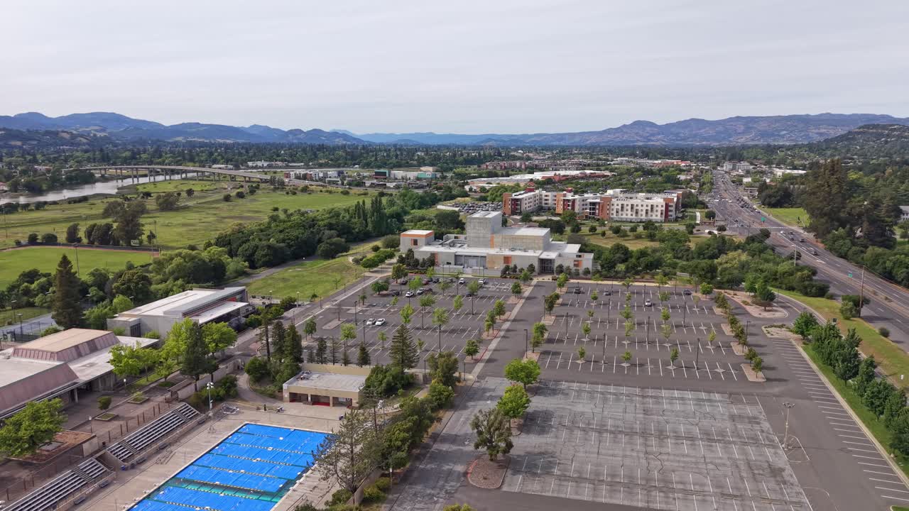Ampia vista aerea panoramica del campus del Napa Valley College a Napa, California, che mostra un parcheggio per lo più vuoto, una piscina coperta, aree verdi e montagne ondulate in lontananza.