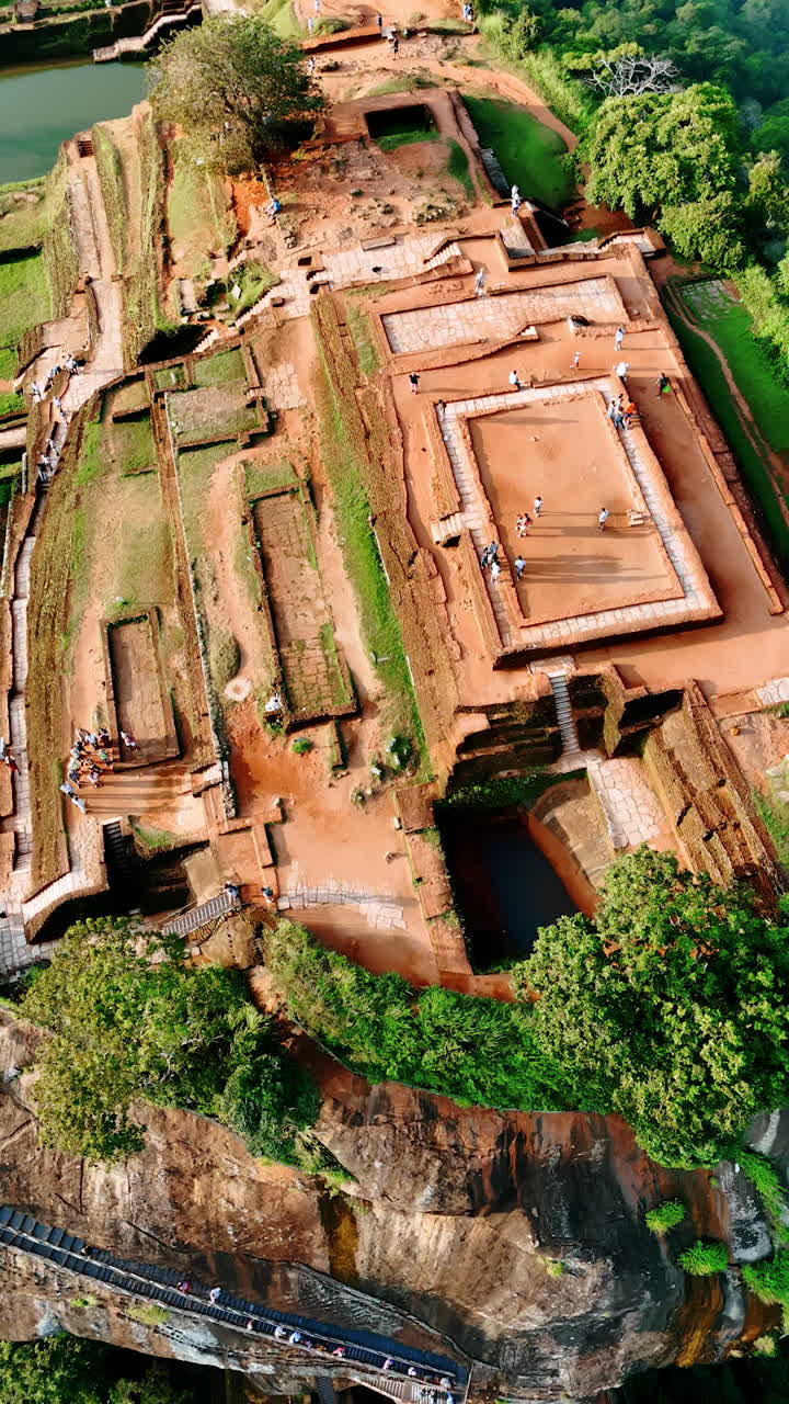 People walk by the ruins of ancient Sigiriya Fortress in Sri Lanka. Drone rising over the top of the mountain. Vertical video.