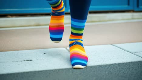 vibrant woman tapping right foot in rainbow socks and blue tights, standing on gray tiled floor near blue door, embodying urban street style with playful energy