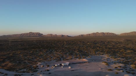 Aerial-view-of-the-dry-Samalayuca-Desert-in-the-state-of-chihuahua-near-Ciudad-Juarez,-El-Paso-Mexico-at-the-US-border-with-view-of-the-dried-landscape-and-mountains-in-the-background-at-golden-hour