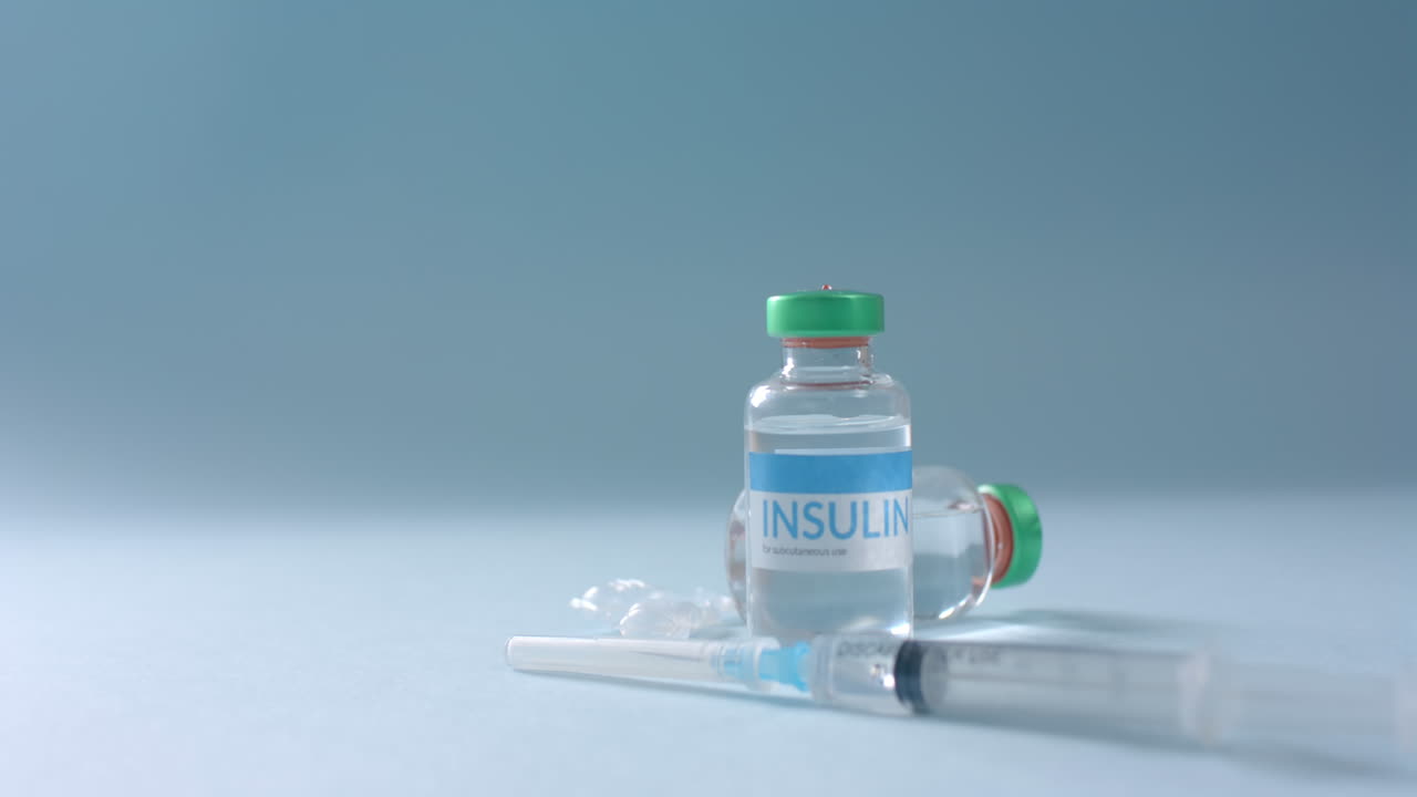Close up of insulin vials and syringe on blue background with copy space, slow motion