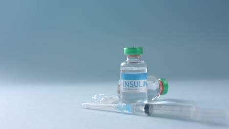 close up of insulin vials and syringe on blue background with copy space, slow motion