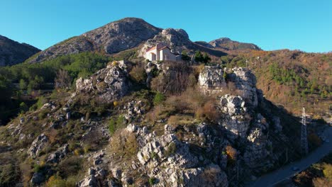 Holy-Church-and-Ancient-Monastery-perched-on-a-towering-rock-in-Rubik,-Albania,-framed-by-majestic-mountains