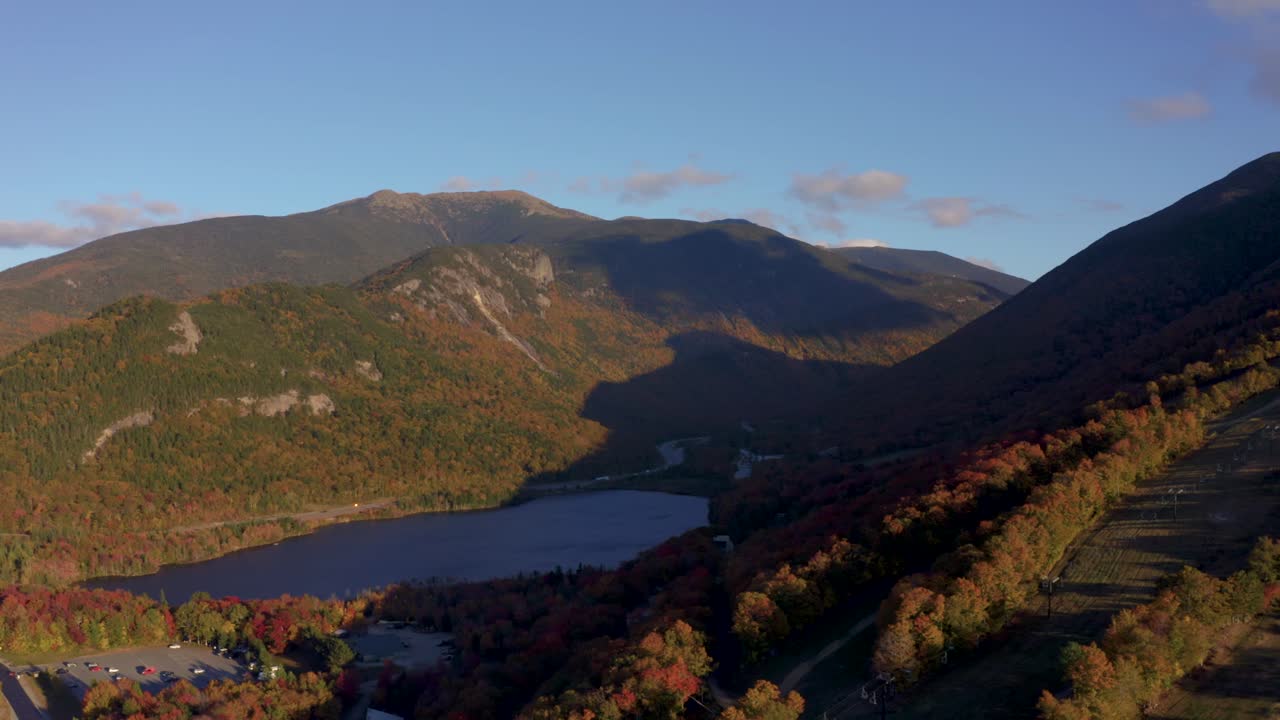 Aerial establishing of Echo Lake and Cannon Mountain surrounded by red and orange fall foliage colors, New Hampshire White mountains