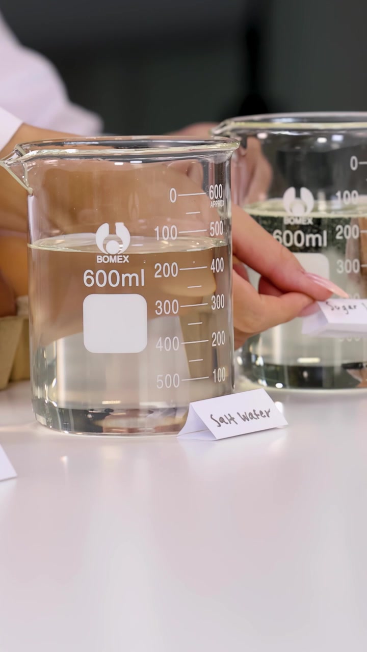 Primo piano di uno studente che sistema etichette per un esperimento sulla densità con becher di vetro e uova.